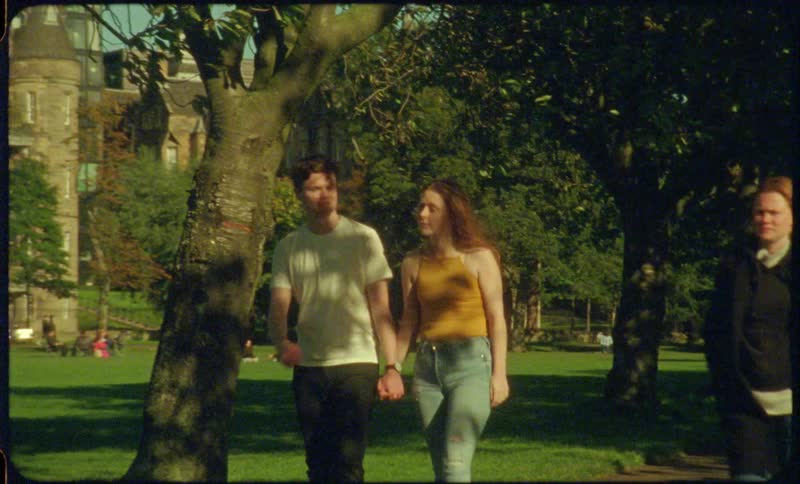 A couple holding hands walking as two people walk by them backwards outdoors in a park during the day