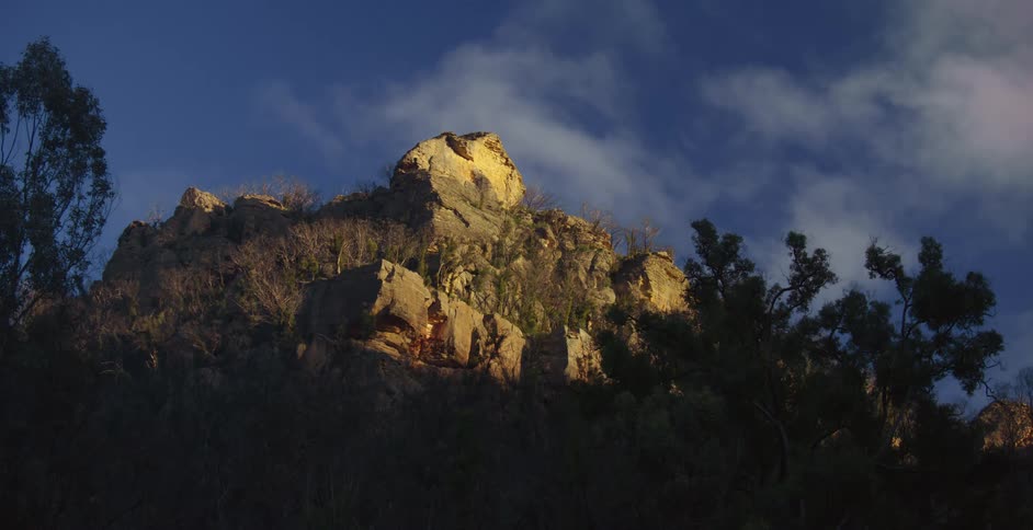 Mountain rock formation with a few trees around and the clouds are passing by
