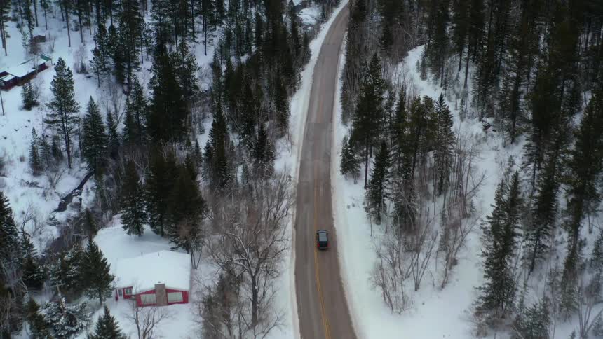 A vehicle driving on a road next to snow and a forest with trees