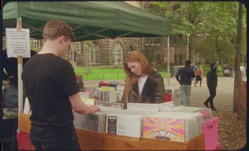 A woman looks up and smiles fondly at the man flipping through records with her at an open market