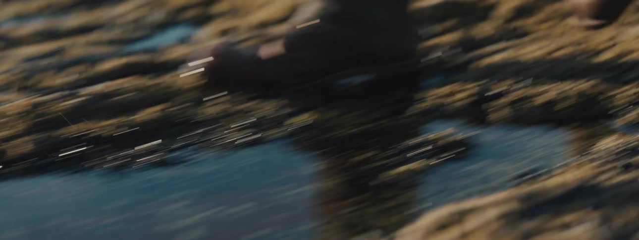 A person walks through puddles on a rocky shore during the day