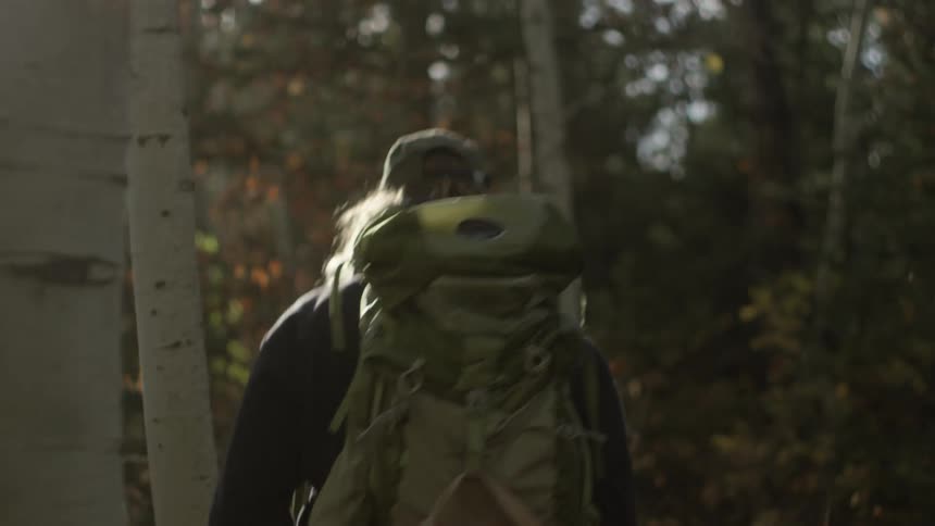 A man with a large backpack hikes through a forested area on a sunny day