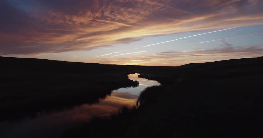 The sun is setting over a dark field with a stream