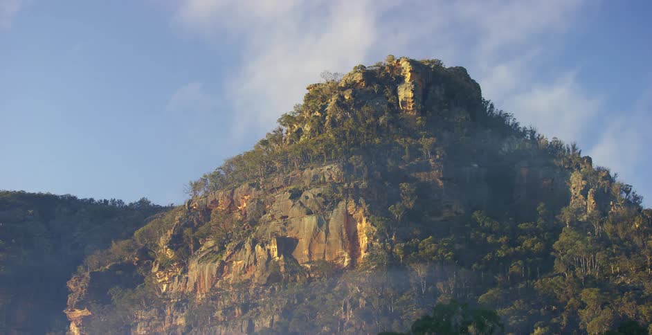 Clouds pass over and the sun shines on tree covered ridge and cliff