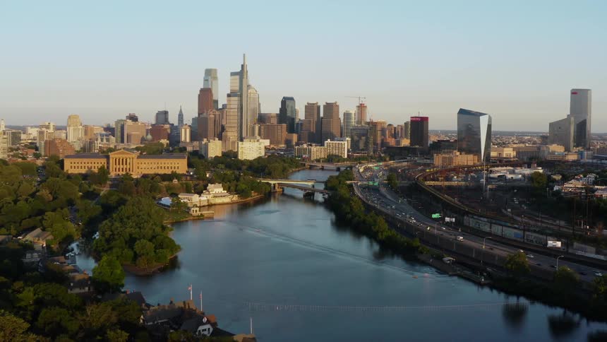 A city full of tall buildings is located next to a large river next to a forested area