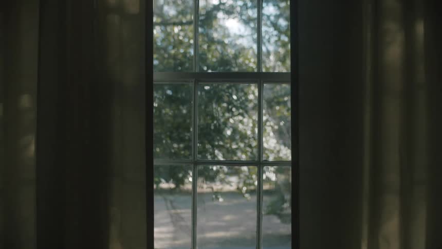 A room with a window and curtains with the american flag trees the sky and clouds in the background