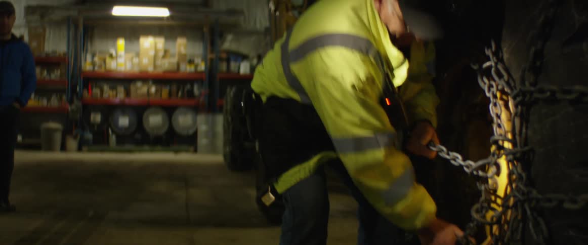 A man works to secure a large chain around the enormous tire of a construction vehicle