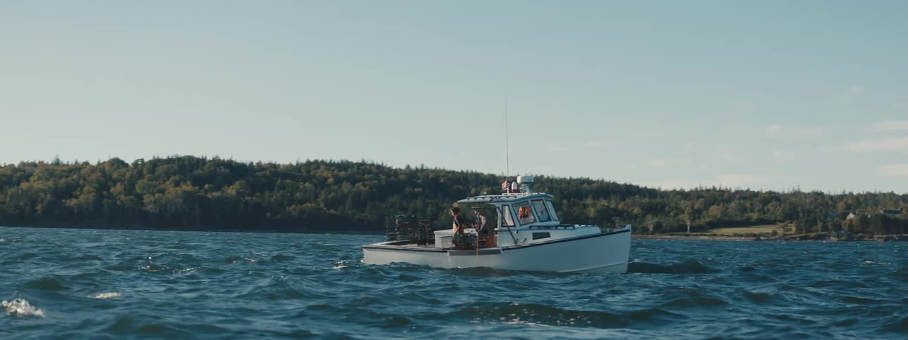 A white boat with two people fishing out in the ocean during the day