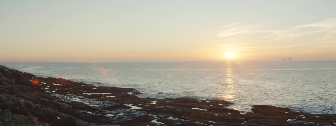A rocky shoreline facing the open ocean as the sun peaks over the horizon