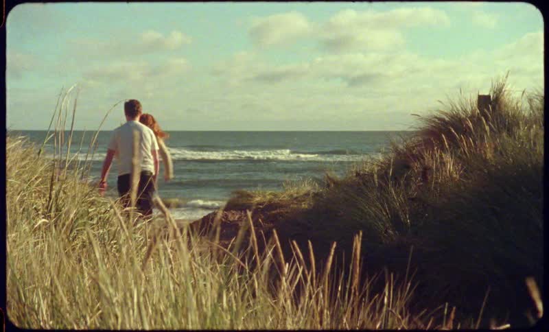 A girl looks back and laughs before running toward the beach while a boy chases her