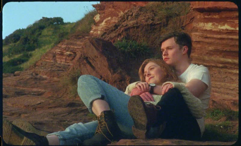 A woman lying back leaning against her boyfriend as they look out over rocky cliff and hill