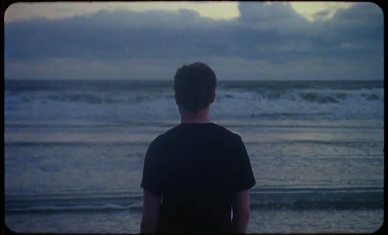 A filmstrip of a male standing on the beach watching the waves roll in