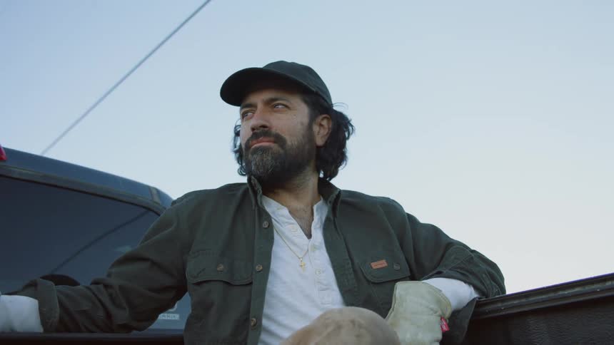 A man sits in the back of a pickup truck as it drives down the street