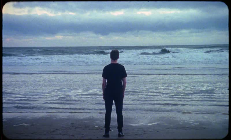 Man in black t shirt and pants watches the wavy sea at dusk on the beach