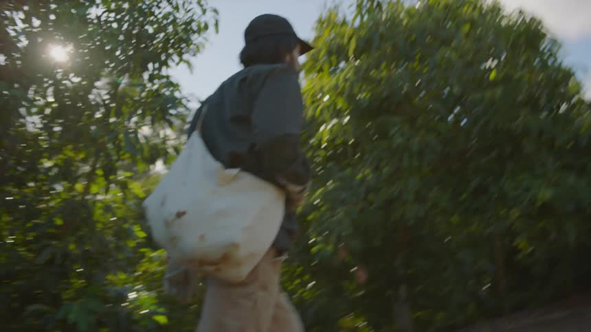 A man with a hat and a bag walking on a dirt road with trees the sky and clouds in the background