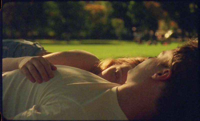 A womans hand lies on her boyfriends chest as they both lay in the grass of a park