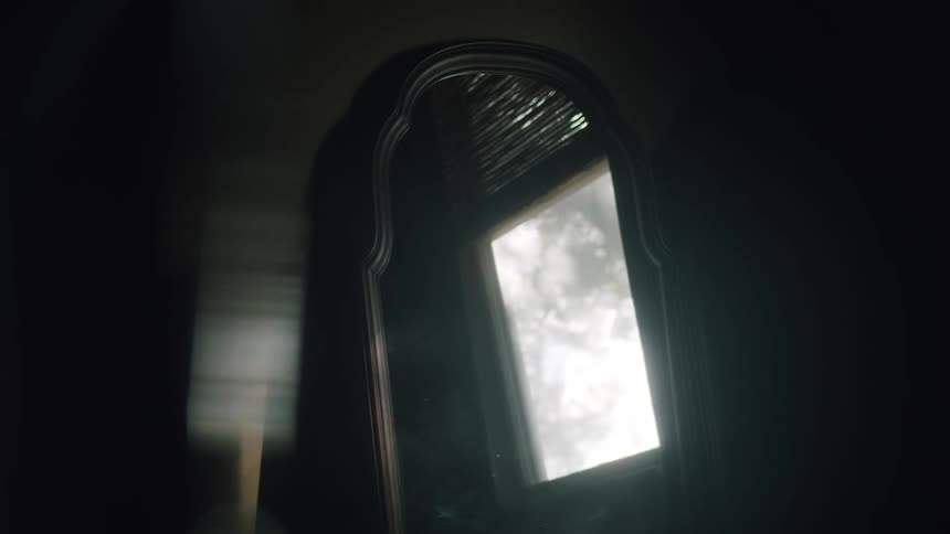 A wall mirror reflects a window with tree branches blowing in the wind