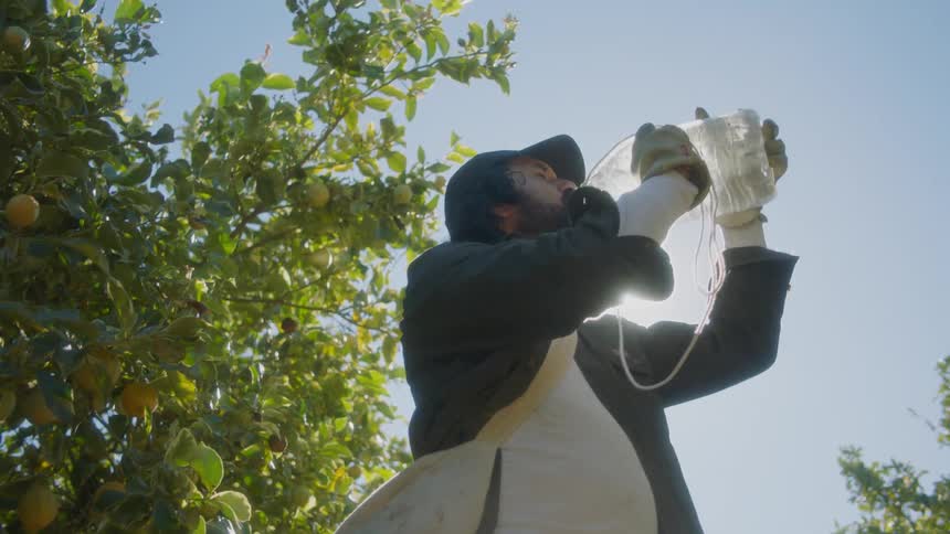 A man with a hat gloves and a bag drinking water from a bottle