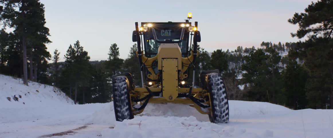 Yellow tractor travels on a snow covered road surrounded by trees
