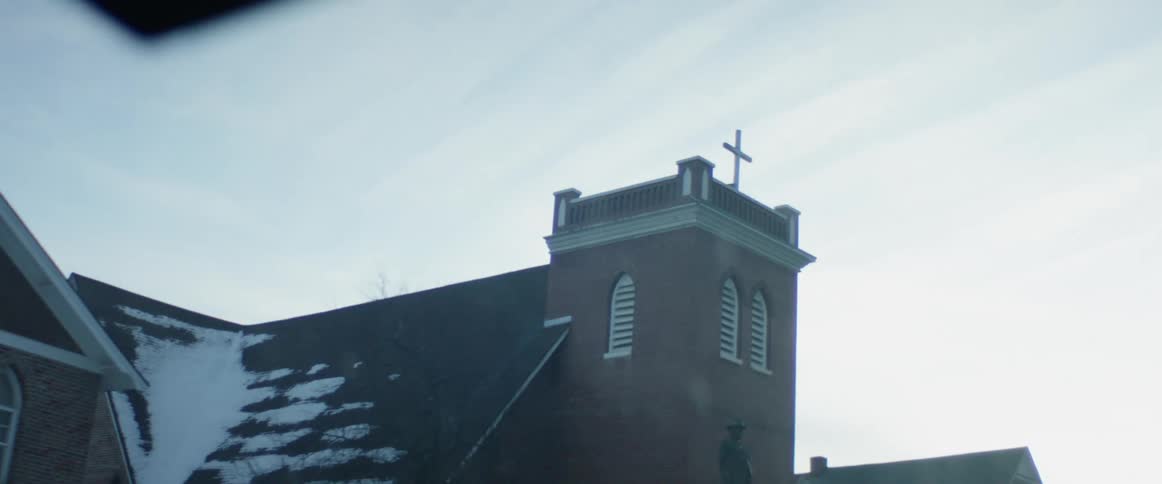 View of a church chapel with a cross on top from the inside of a moving vehicle during the day