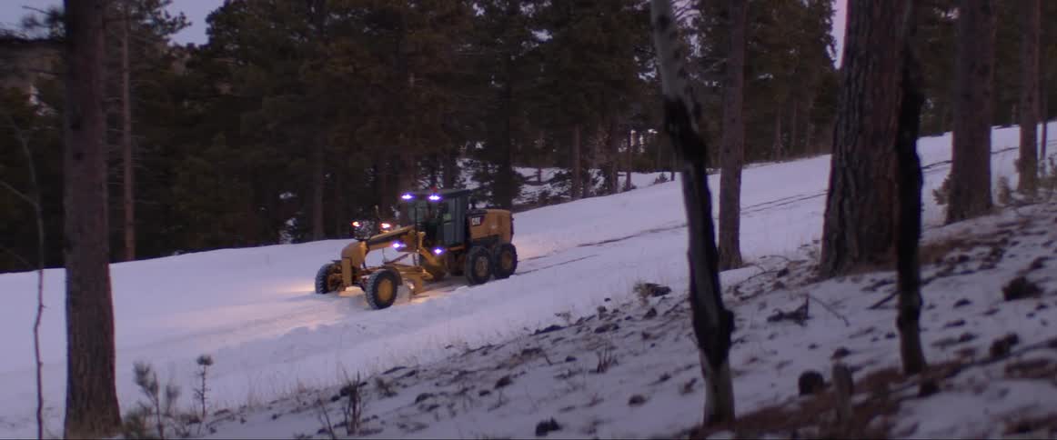 Commercial vehicle moves along snow covered road between conifer trees