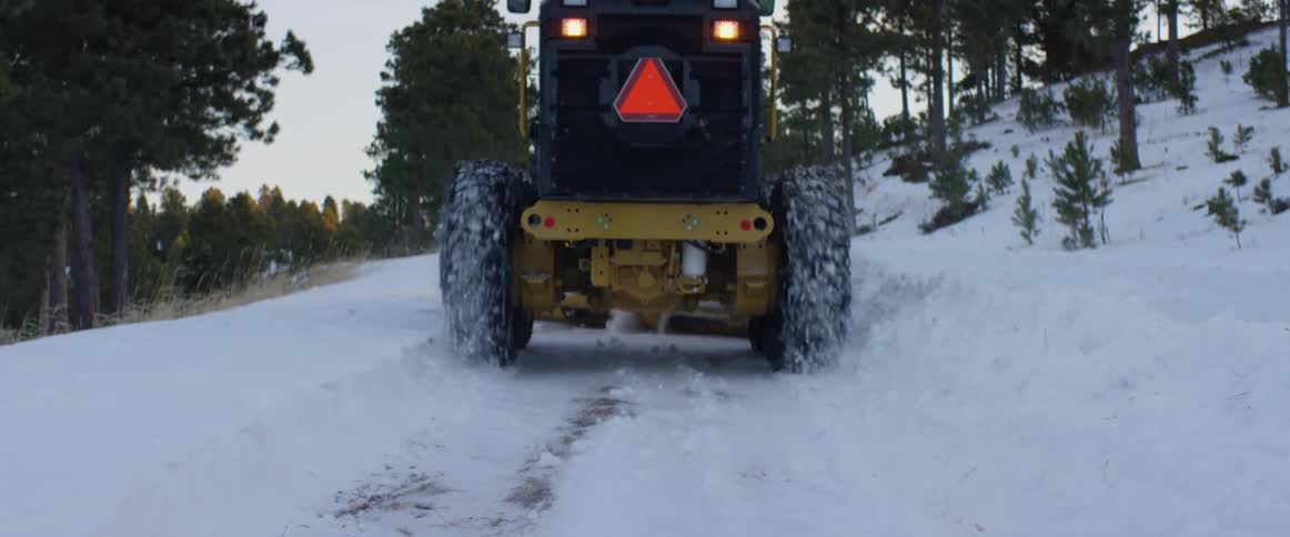 A large snowplow vehicle drives slowly along a snow covered path