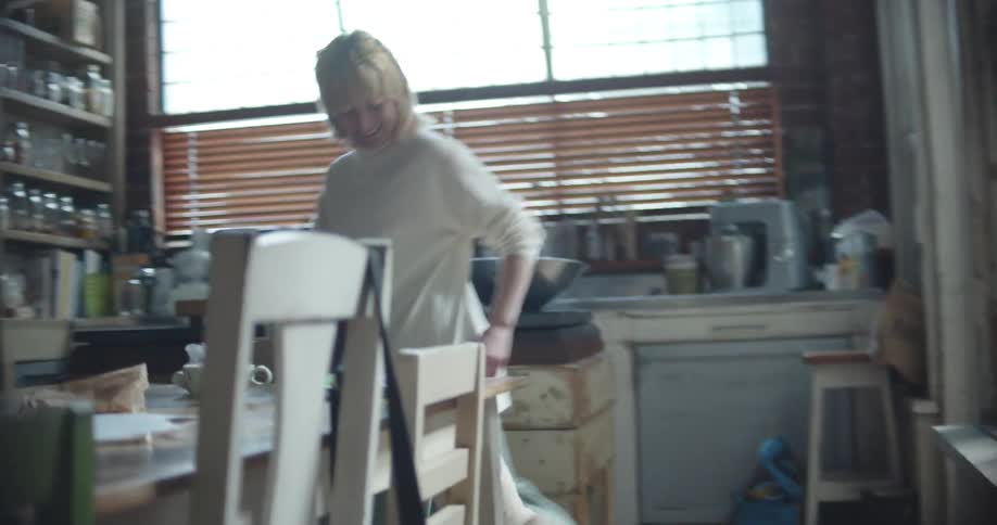 A woman plays with a white dog at home running through the living room and kitchen during the day