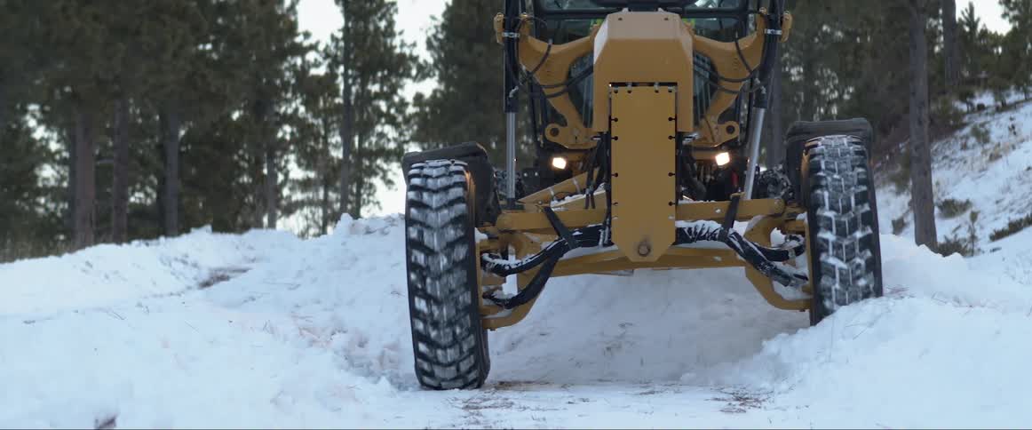 A tractor driving on snow and ice with trees the sky and clouds in the background