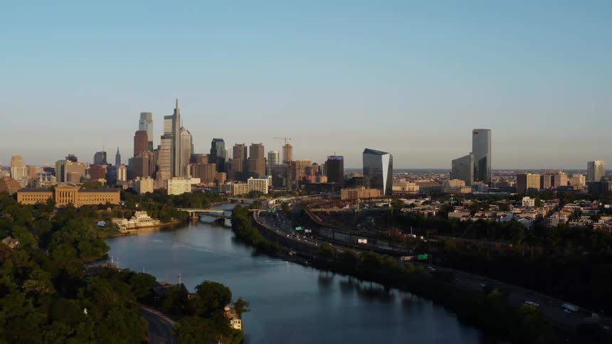The Philadelphia skyline in the distance with a waterway and a highway down below where cars are driving by