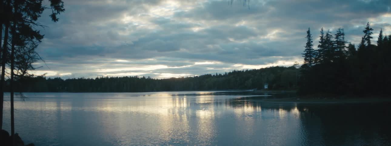 Sunlight peaks through heavy clouds and shines onto a calm lake
