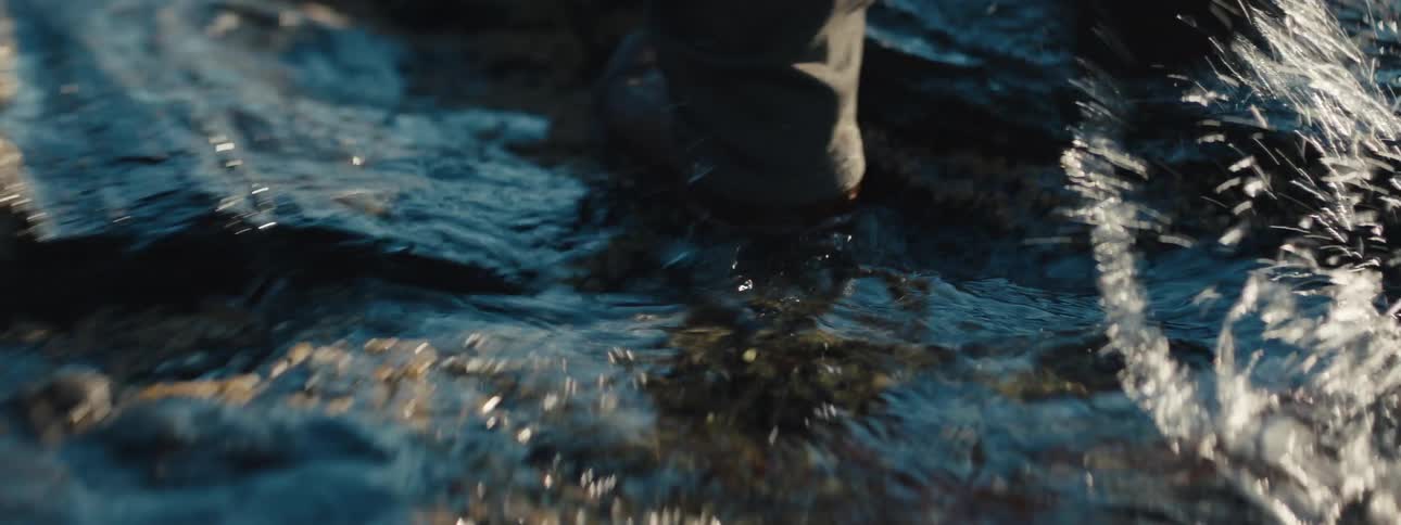 A person walks through puddles on a rock shoreline during the day
