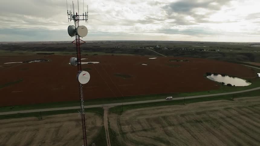 Very tall communication antenna sitting high on a tower in a rural area