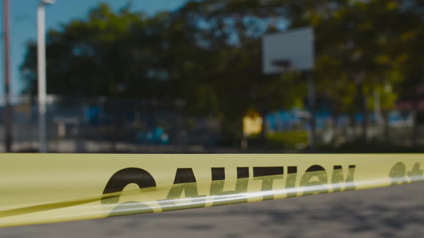 Yellow caution tape blocks off a basketball court outdoors