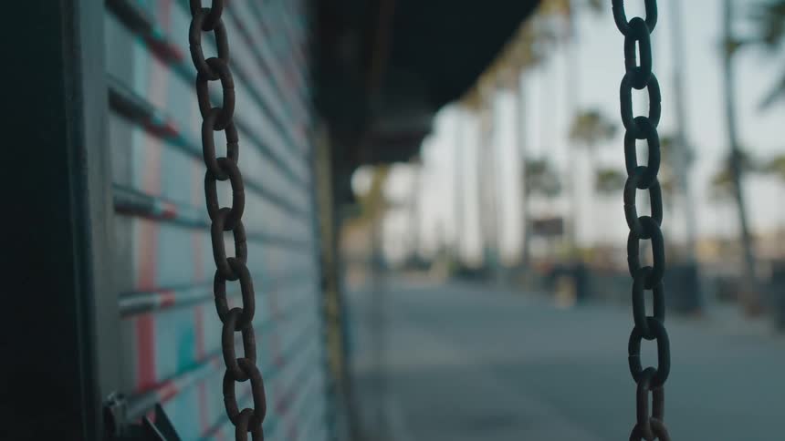A pair of chains dangle from a building located near a walkway lined with palm trees