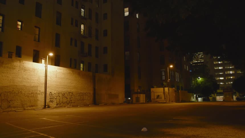 An empty parking lot is shown in a city at night
