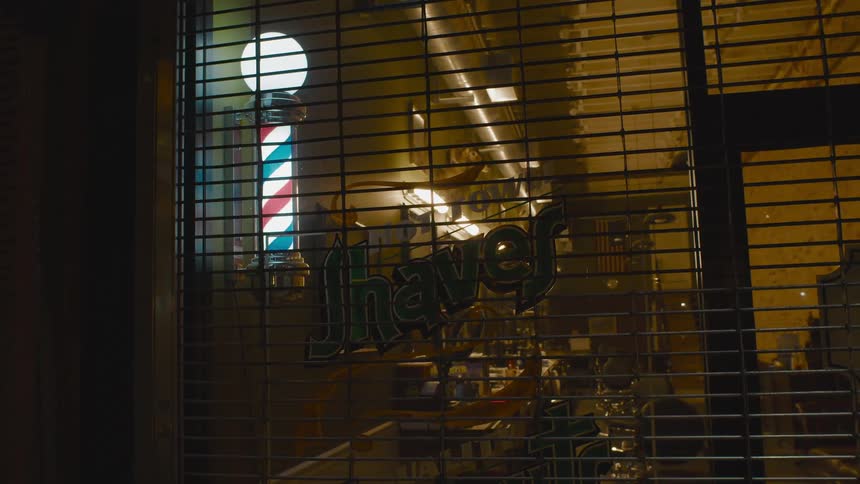 The front of a closed barbershop protected by a security gate at night
