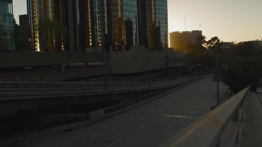 Building facades reflect the glowing sun and surrounding buildings beside an empty highway