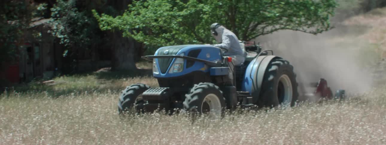 A person drives a tractor that is dragging an apparatus for turning the soil