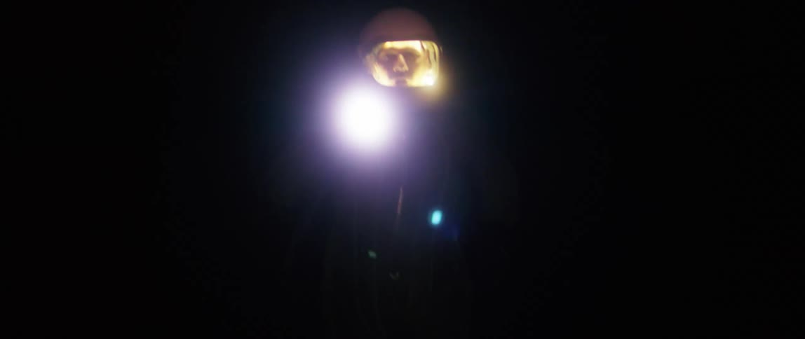 A person with a spacesuit and flashlight running in the dark