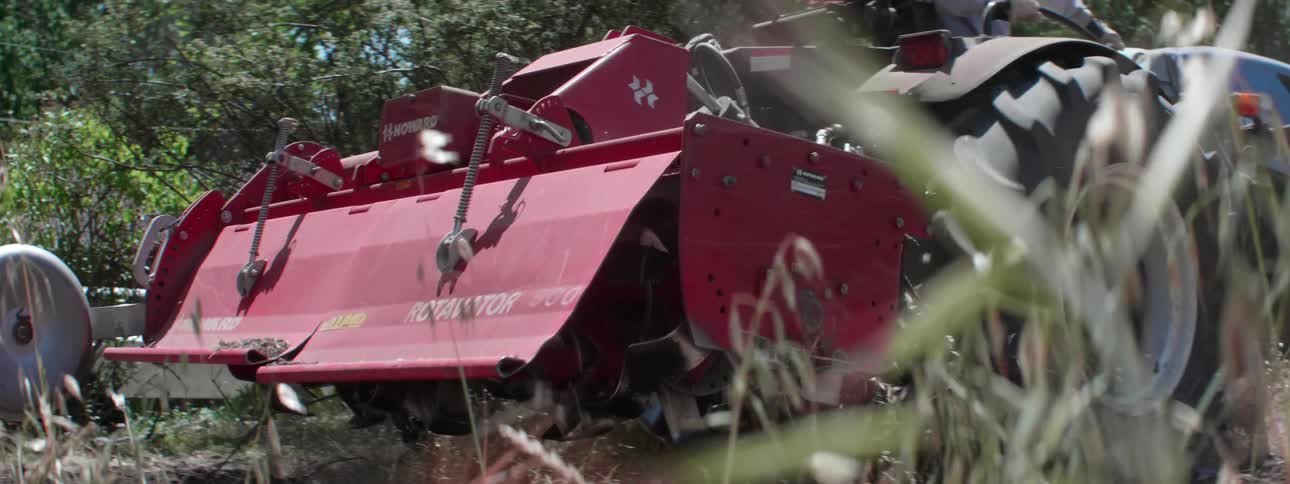 A farmer backs a tractor with tiller attachment to a fence and stops