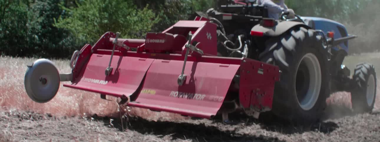 A farmer plowing a dirt field on a sunny day