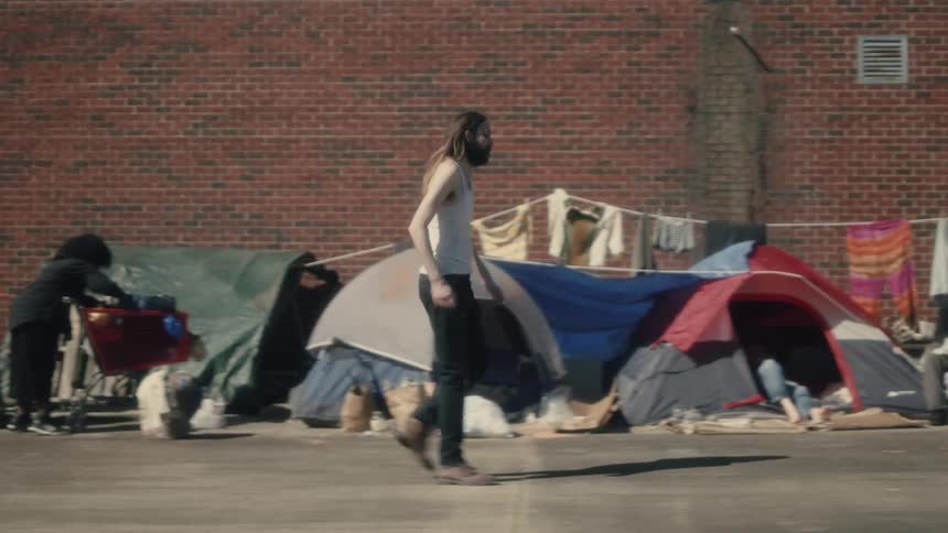 A man pumps his fist in excitement as he walks through a homeless camp