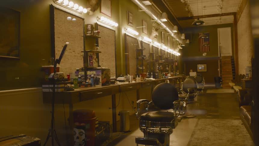 The lights are on inside an empty barber shop with chairs all turned in the same direction