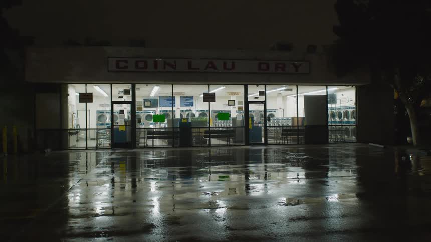 Lights glowing inside a laundromat during a rainstorm at night