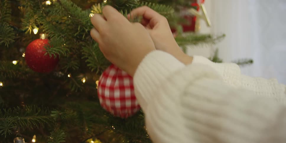 A person in a room putting an ornament on a christmas tree with a wall in the background