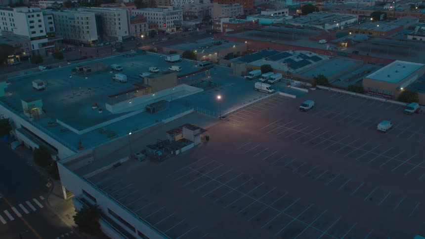 Cars and vans parked on rooftop lots with city lights glowing at dusk