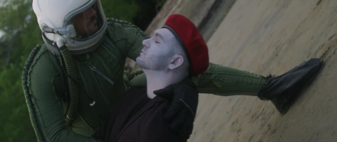 A man with a helmet on grabs and lowers another man to the ground as he appears to faint