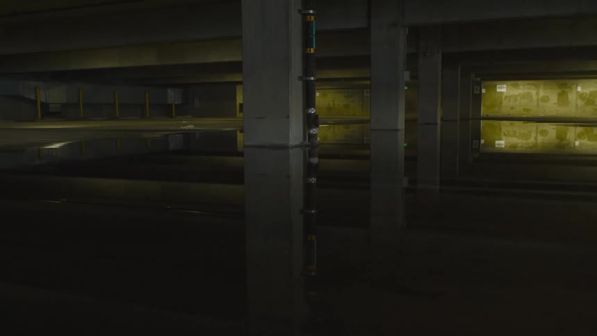 Puddles on the floor reflect the columns and papered windows in an empty garage or warehouse