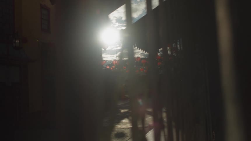 Sun shines into narrow road between buildings with red lanterns hung over street
