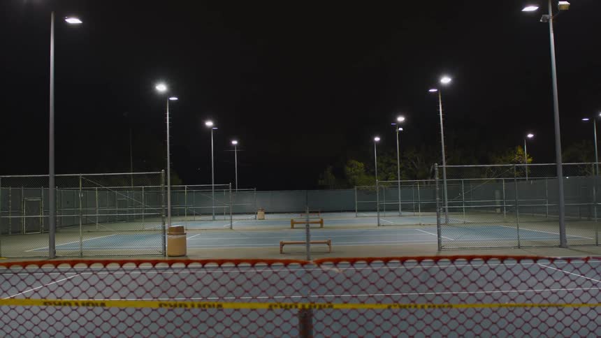 Caution tape flutters near sports courts at night